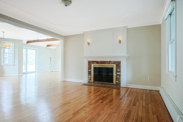 unfurnished living room featuring light wood finished floors, a brick fireplace, baseboards, beamed ceiling, and baseboard heating