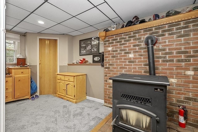 detailed view of a fire extinguisher, a wood stove, baseboards, carpet, and a drop ceiling
