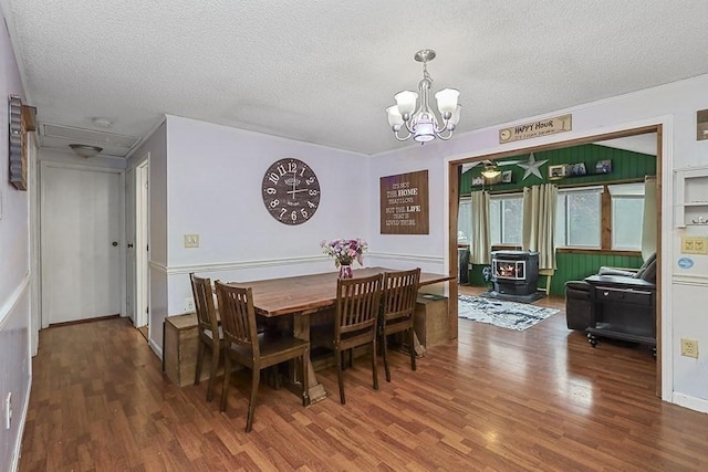 dining space featuring wood finished floors, a chandelier, a textured ceiling, and a wood stove