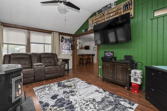 living room with a ceiling fan, wood finished floors, a wood stove, vaulted ceiling, and wooden walls