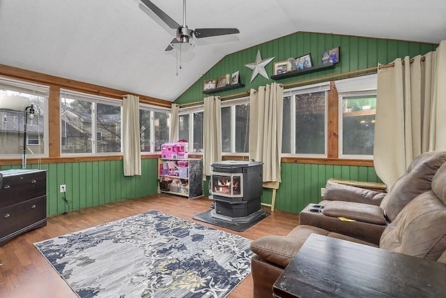 sunroom / solarium featuring lofted ceiling, a wood stove, wood finished floors, a deck, and wood walls