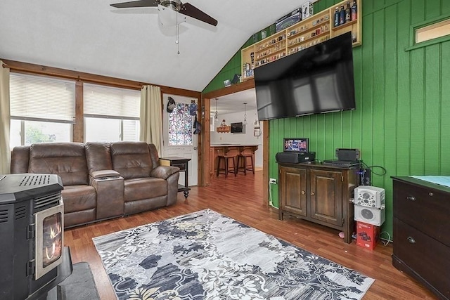 living room with ceiling fan, wood finished floors, vaulted ceiling, and a wood stove