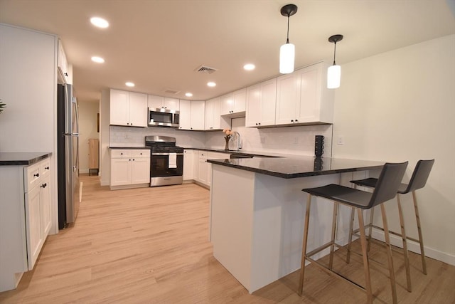 kitchen with stainless steel appliances, hanging light fixtures, a peninsula, and white cabinets