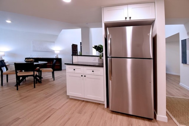 kitchen featuring dark stone counters, light wood finished floors, freestanding refrigerator, and white cabinetry