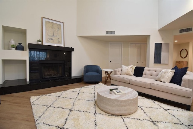 living area with a high ceiling, visible vents, wood finished floors, and a tile fireplace