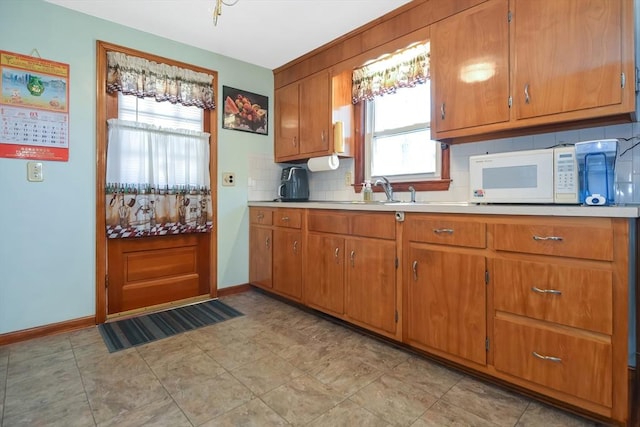 kitchen featuring white microwave, tasteful backsplash, light countertops, brown cabinetry, and a sink