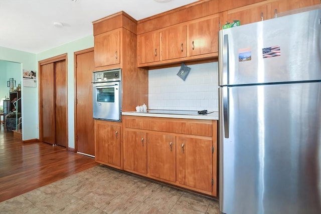 kitchen with stainless steel appliances, backsplash, brown cabinetry, and light countertops