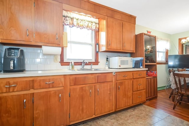 kitchen with white microwave, brown cabinetry, light countertops, and a sink