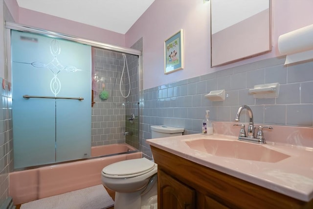 bathroom featuring vanity, tile walls, toilet, and bath / shower combo with glass door