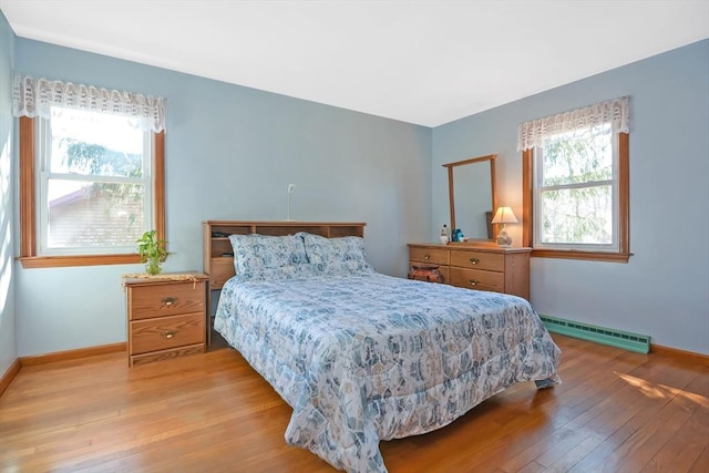 bedroom with a baseboard heating unit, hardwood / wood-style flooring, multiple windows, and baseboards