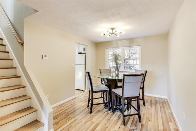 dining area featuring a textured ceiling, a notable chandelier, and light wood-type flooring