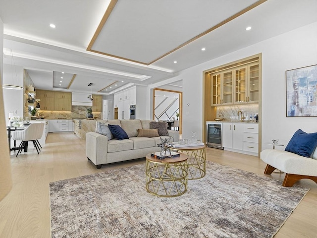 living room featuring beverage cooler, light hardwood / wood-style flooring, bar, and a raised ceiling