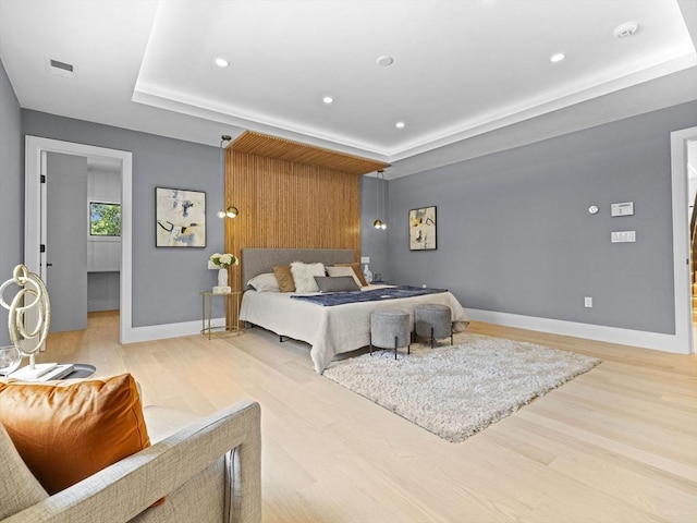 bedroom with light hardwood / wood-style floors and a tray ceiling