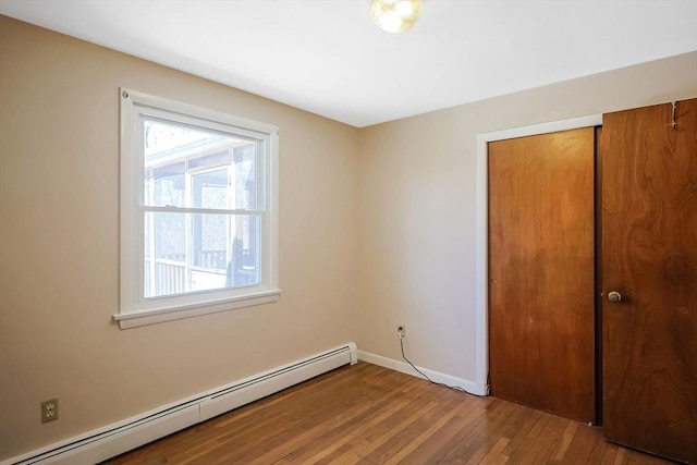 unfurnished bedroom featuring a baseboard heating unit, wood finished floors, baseboards, and a closet