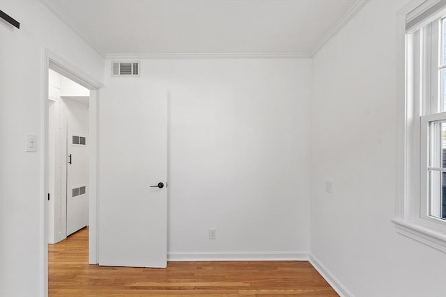 empty room featuring visible vents, light wood-style floors, and crown molding