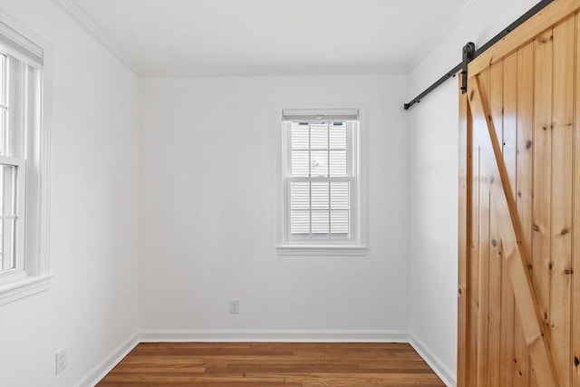 unfurnished room with crown molding, baseboards, a barn door, and wood finished floors