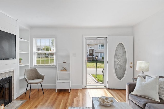 living room featuring a fireplace with flush hearth, built in shelves, wood finished floors, baseboards, and ornamental molding