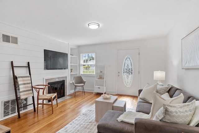 living area with visible vents, a fireplace with flush hearth, built in shelves, and light wood-type flooring