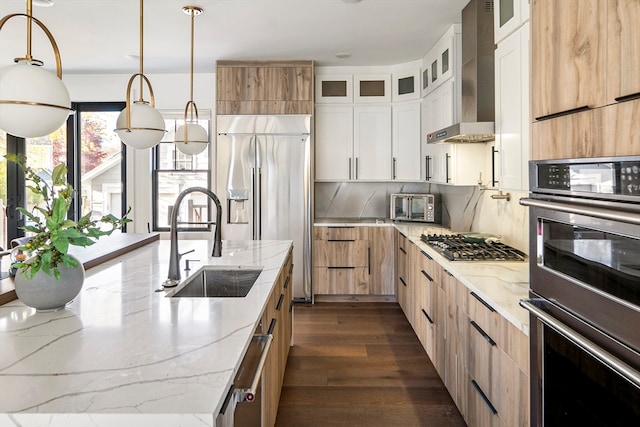 kitchen featuring pendant lighting, white cabinets, wall chimney range hood, sink, and appliances with stainless steel finishes