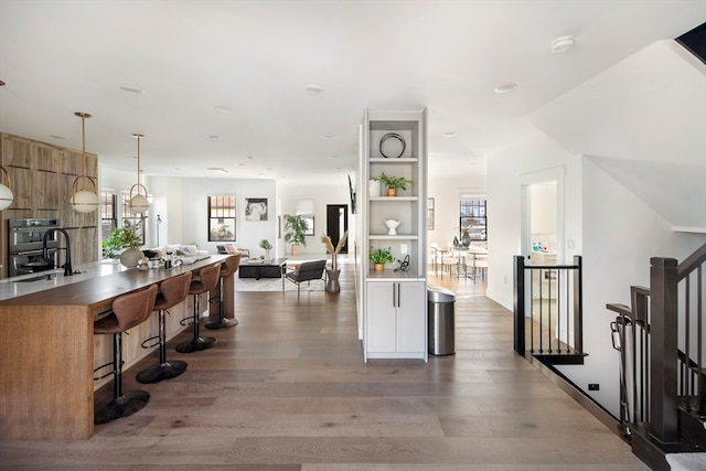 interior space featuring sink, stainless steel double oven, a kitchen breakfast bar, dark hardwood / wood-style floors, and pendant lighting