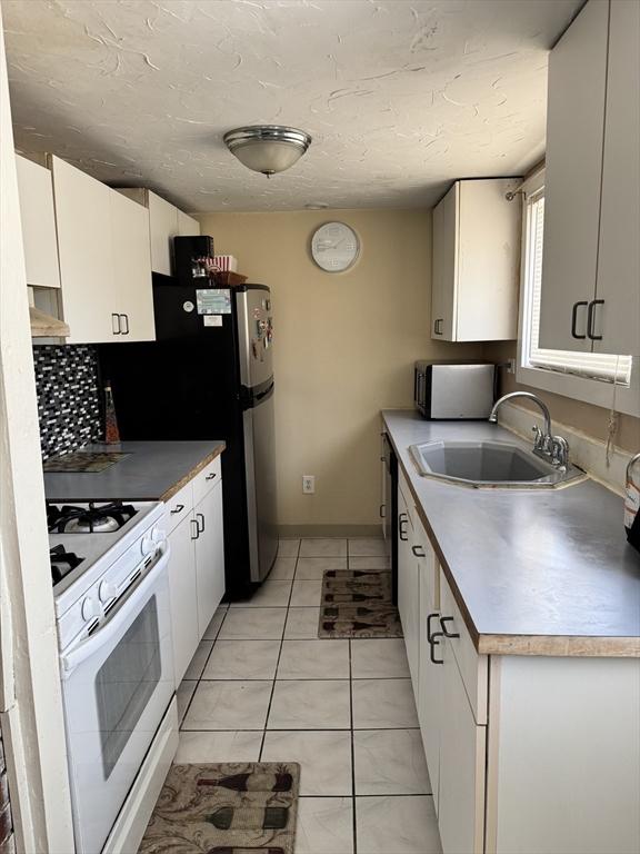 kitchen with light tile patterned floors, white gas range oven, white cabinets, and a sink