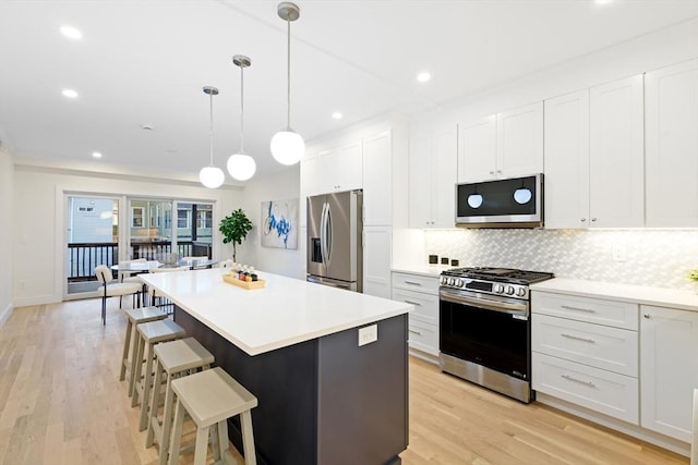 kitchen with white cabinetry, decorative light fixtures, a kitchen island, and appliances with stainless steel finishes