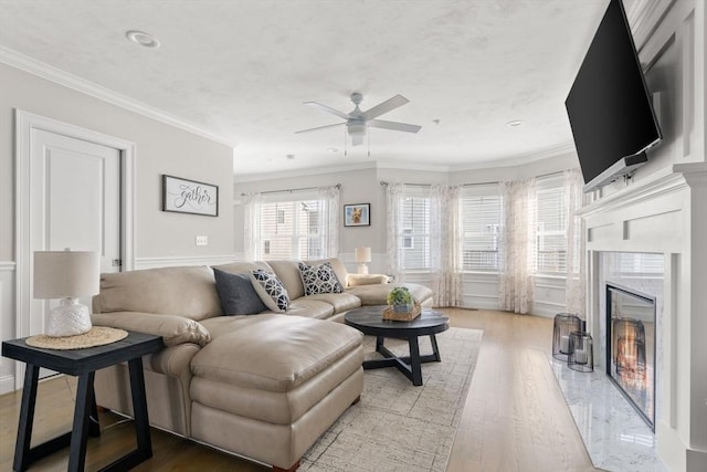 living room featuring a ceiling fan, crown molding, a premium fireplace, and wood finished floors