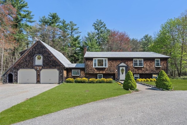 bi-level home featuring a chimney, an attached garage, driveway, and a front lawn