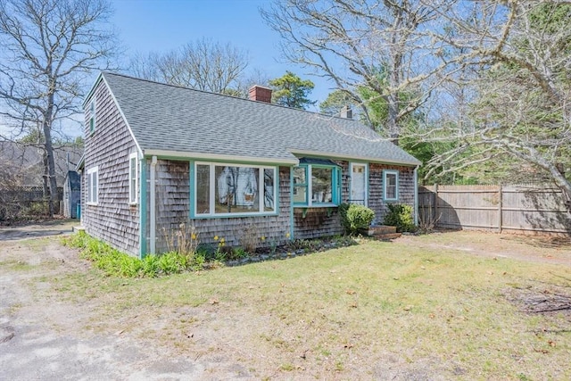 25 Charlotte Ave, Barnstable, MA 02635 - view of front facade with a front yard, roof with shingles, fence, and a chimney