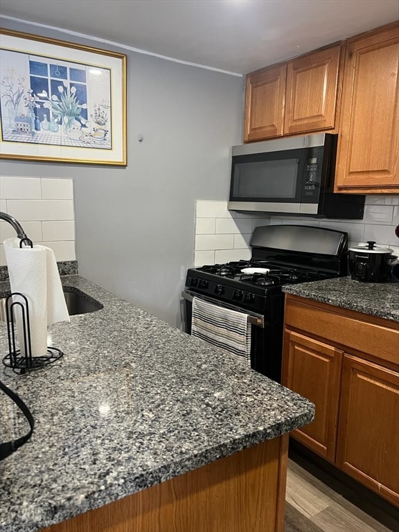 kitchen with range with gas cooktop, tasteful backsplash, dark stone countertops, and light hardwood / wood-style flooring