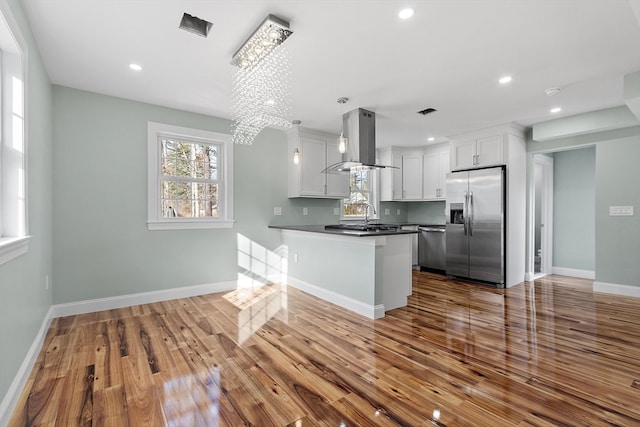 kitchen with island exhaust hood, kitchen peninsula, stainless steel appliances, hardwood / wood-style flooring, and white cabinets