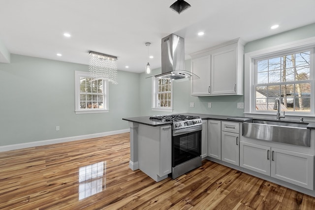 kitchen with pendant lighting, kitchen peninsula, stainless steel gas stove, island range hood, and white cabinetry