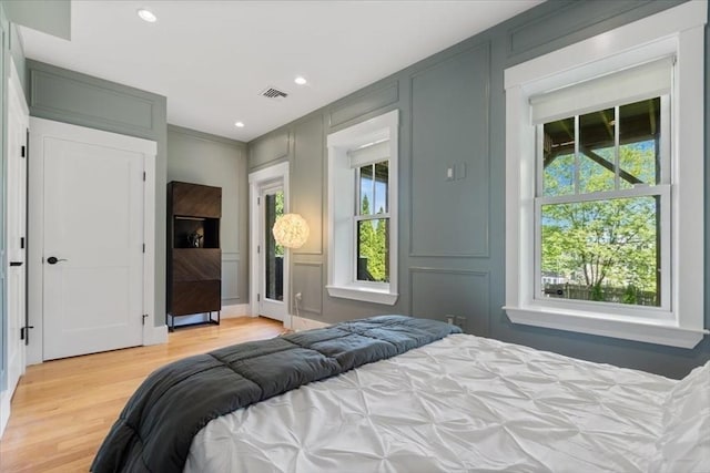 bedroom featuring multiple windows, light wood-type flooring, a decorative wall, and recessed lighting