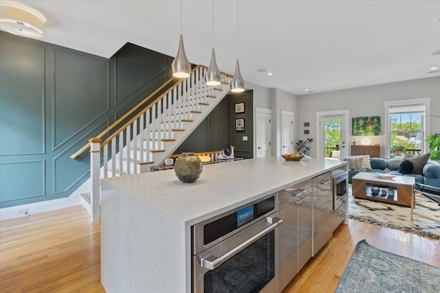 kitchen featuring oven, light wood-type flooring, a center island, open floor plan, and light countertops