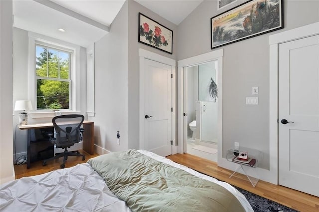 bedroom with wood finished floors, baseboards, lofted ceiling, ensuite bath, and a desk