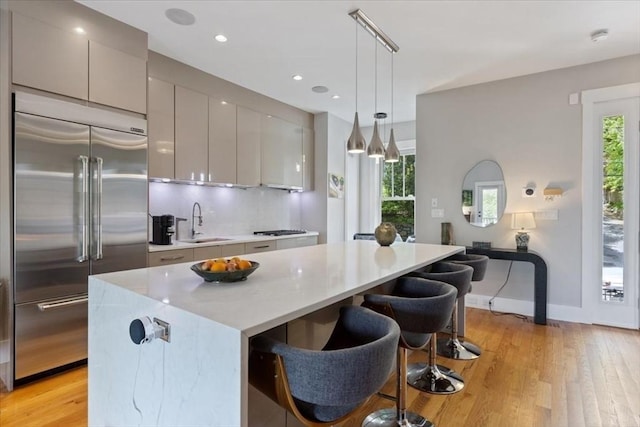 kitchen featuring built in refrigerator, a sink, gray cabinets, light wood-type flooring, and a center island
