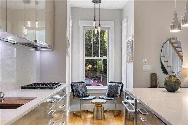 kitchen featuring gas stovetop, hanging light fixtures, exhaust hood, baseboards, and light wood finished floors