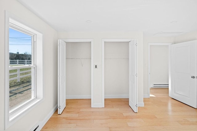 unfurnished bedroom featuring a baseboard radiator, multiple closets, and light wood-type flooring