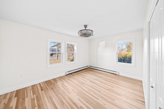 spare room featuring baseboard heating, light wood-type flooring, and a healthy amount of sunlight