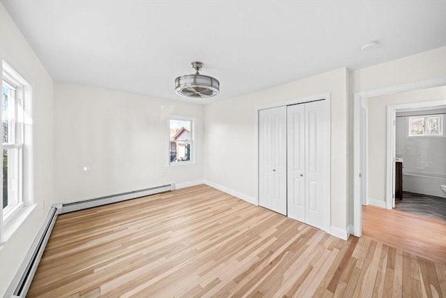 unfurnished bedroom with a closet, a baseboard heating unit, and light hardwood / wood-style floors