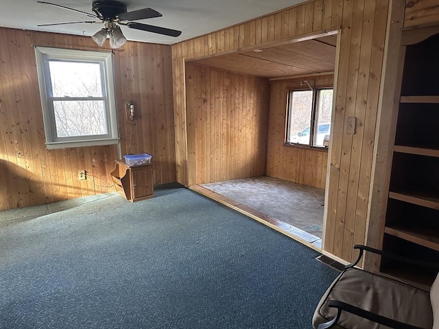 empty room featuring ceiling fan, carpet, and wood walls