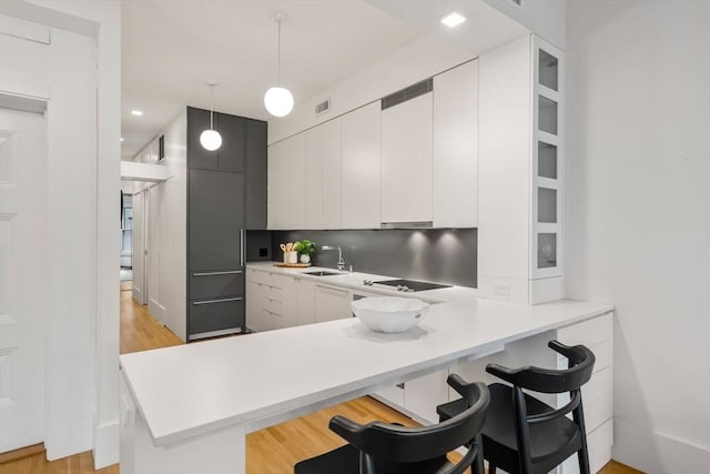 kitchen with light wood-type flooring, kitchen peninsula, a kitchen bar, white cabinetry, and decorative light fixtures