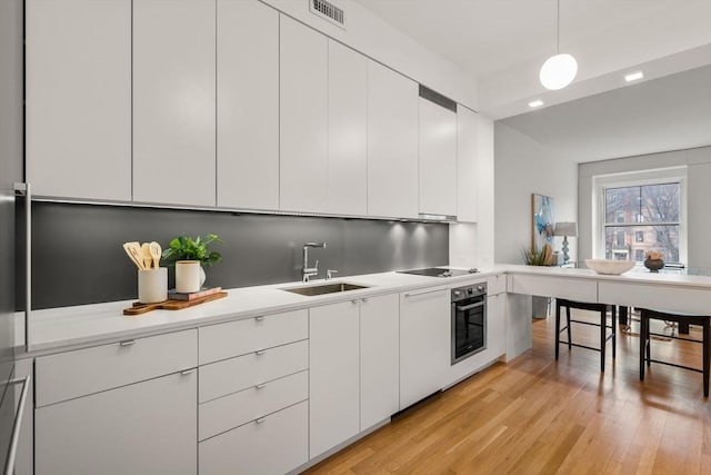 kitchen with sink, pendant lighting, black electric cooktop, and white cabinetry