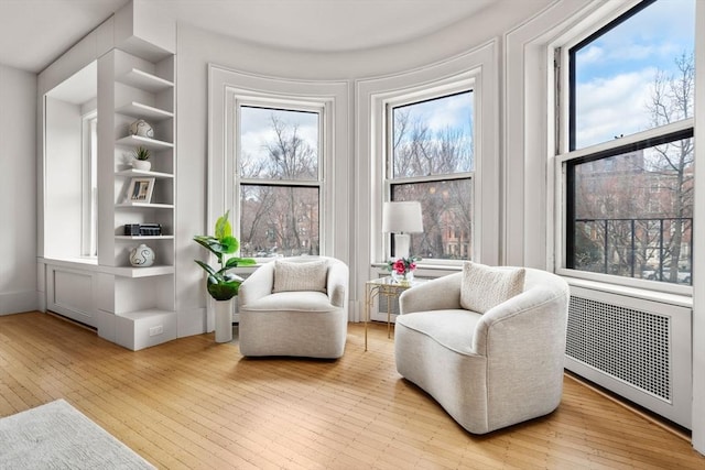 sitting room featuring built in shelves, light hardwood / wood-style flooring, and radiator heating unit