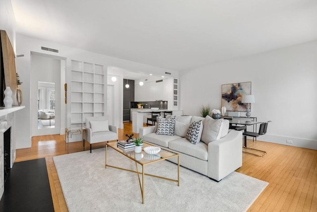 living room featuring a premium fireplace, light hardwood / wood-style flooring, and built in shelves