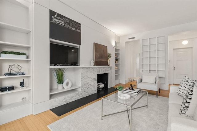 living room with built in shelves, a premium fireplace, and hardwood / wood-style floors