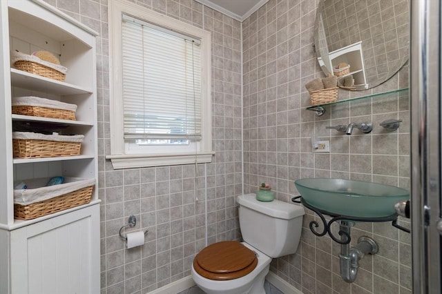 bathroom with crown molding, toilet, and tile walls