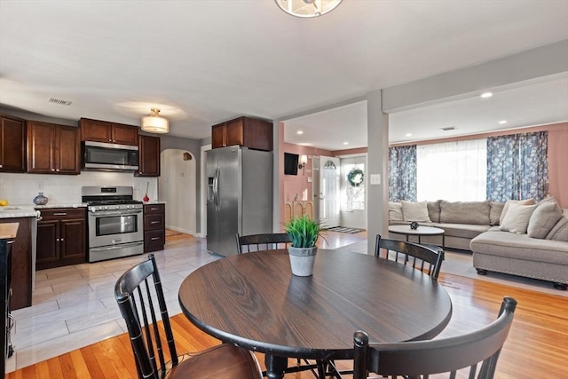 dining space featuring light wood-type flooring, visible vents, arched walkways, and recessed lighting