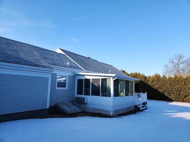 snow covered back of property featuring a sunroom