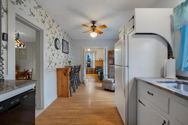 14 Cottage St, Whitman, MA 02382 - kitchen with black dishwasher, wallpapered walls, light wood-style flooring, white cabinetry, and ceiling fan
